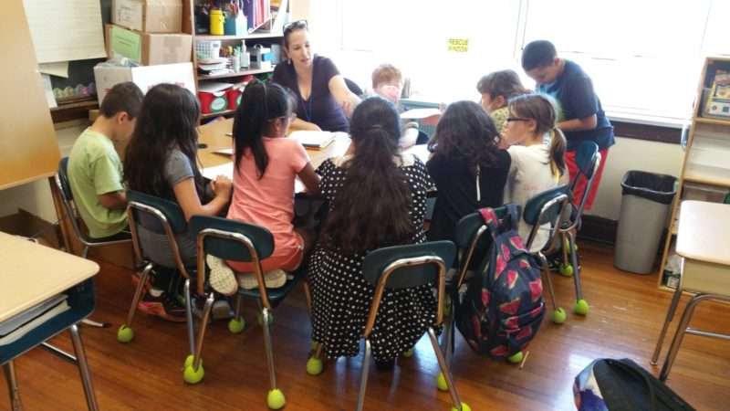 Children sitting at a round table in a classroom working with a teacher